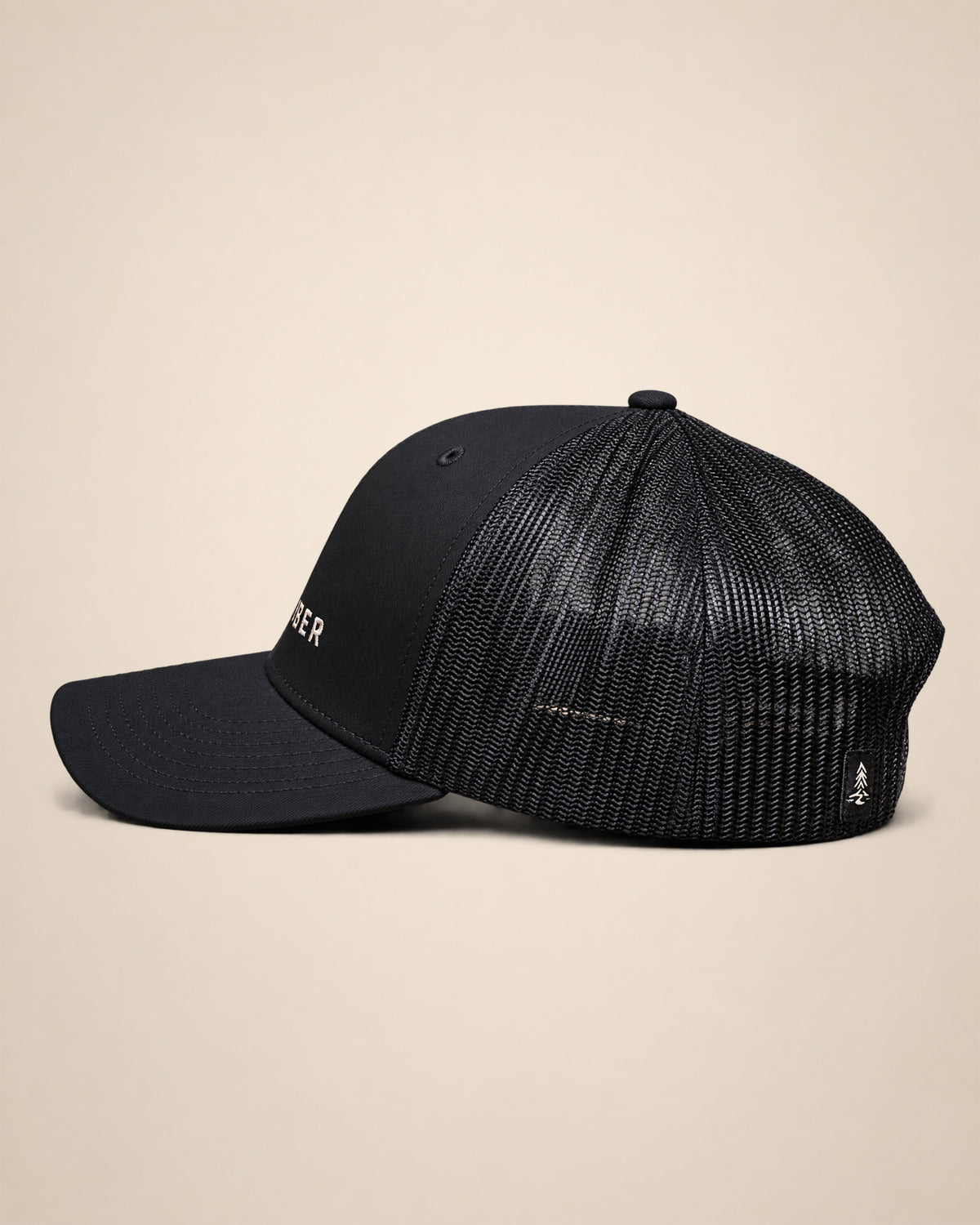 Side view of the black Timber Mark trucker hat showing the mesh back and rear woven Black Timber detail.