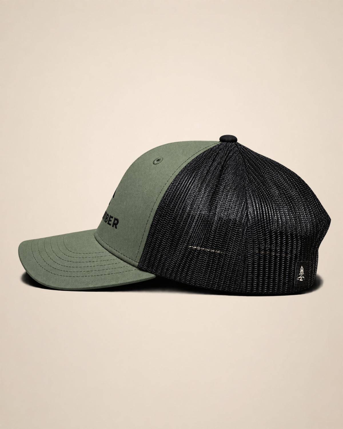 Side view of the olive Timber Mark trucker hat showing the mesh back and rear woven Black Timber detail.